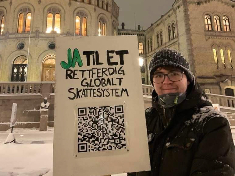 Mann kledd i lue og jakke står med plakat foran Stortinget.
