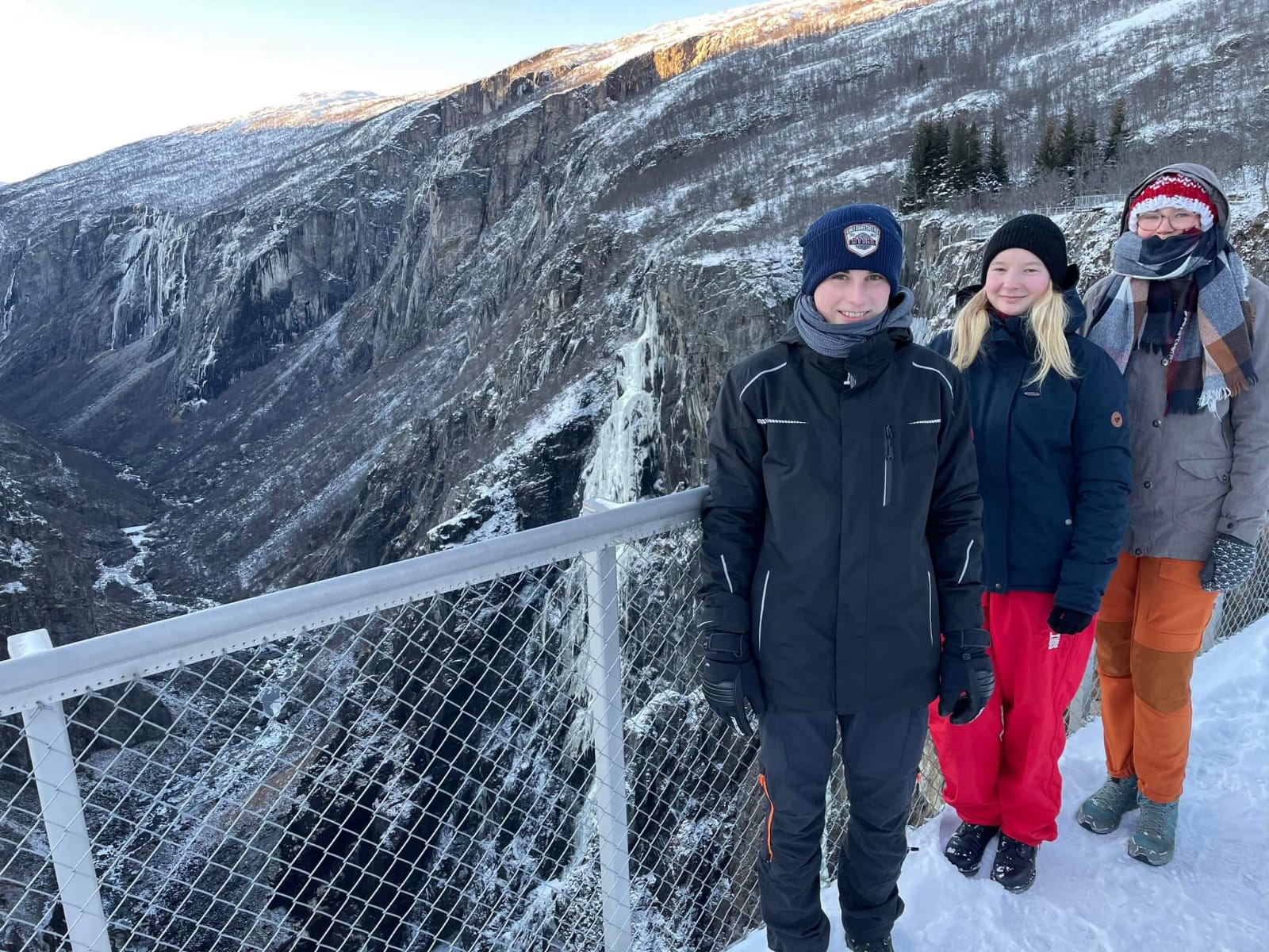 Foto av tre personer ved et gjerde. Bratt stup på andre siden av gjerdet.